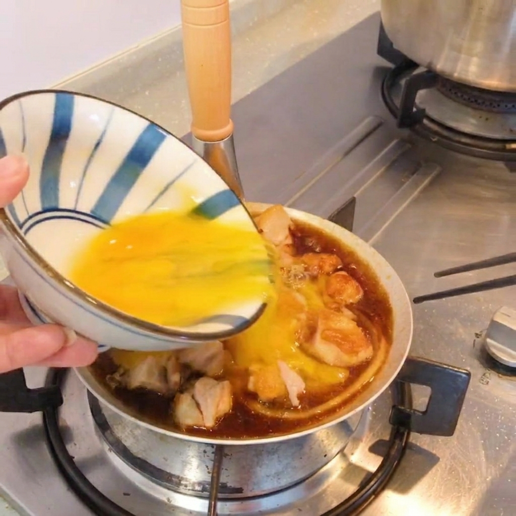 팬에 담긴 완성된 오야코동 위에 쪽파를 뿌리는 모습.