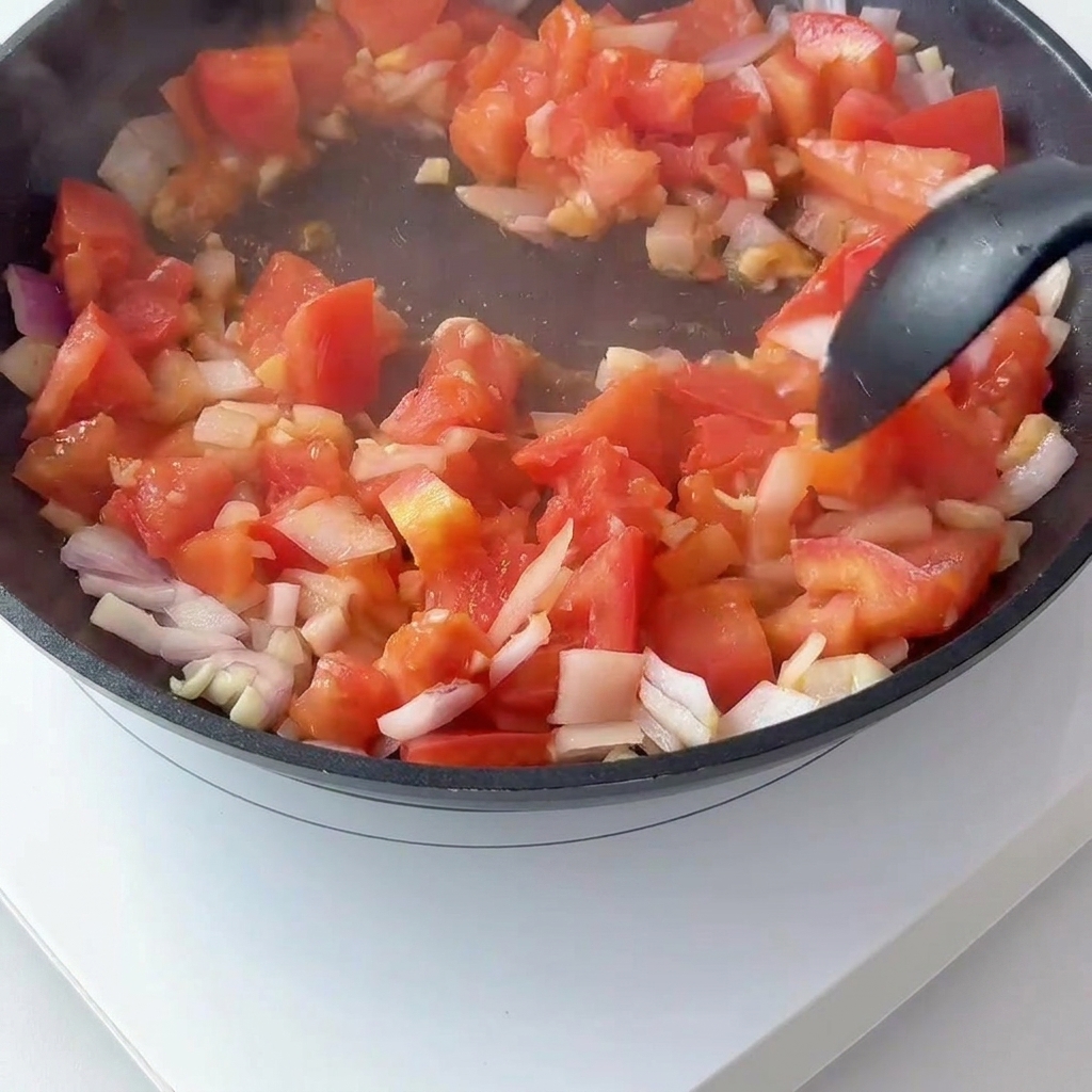 팬에서 볶은 토마토와 양파에 토마토 페이스트를 섞는 모습.