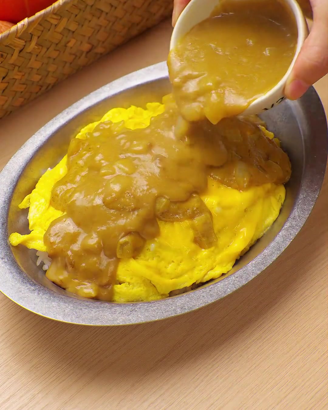 작은 그릇에 담긴 진한 노란색 카레 소스를 스크램블 에그와 밥 위에 붓는 모습.