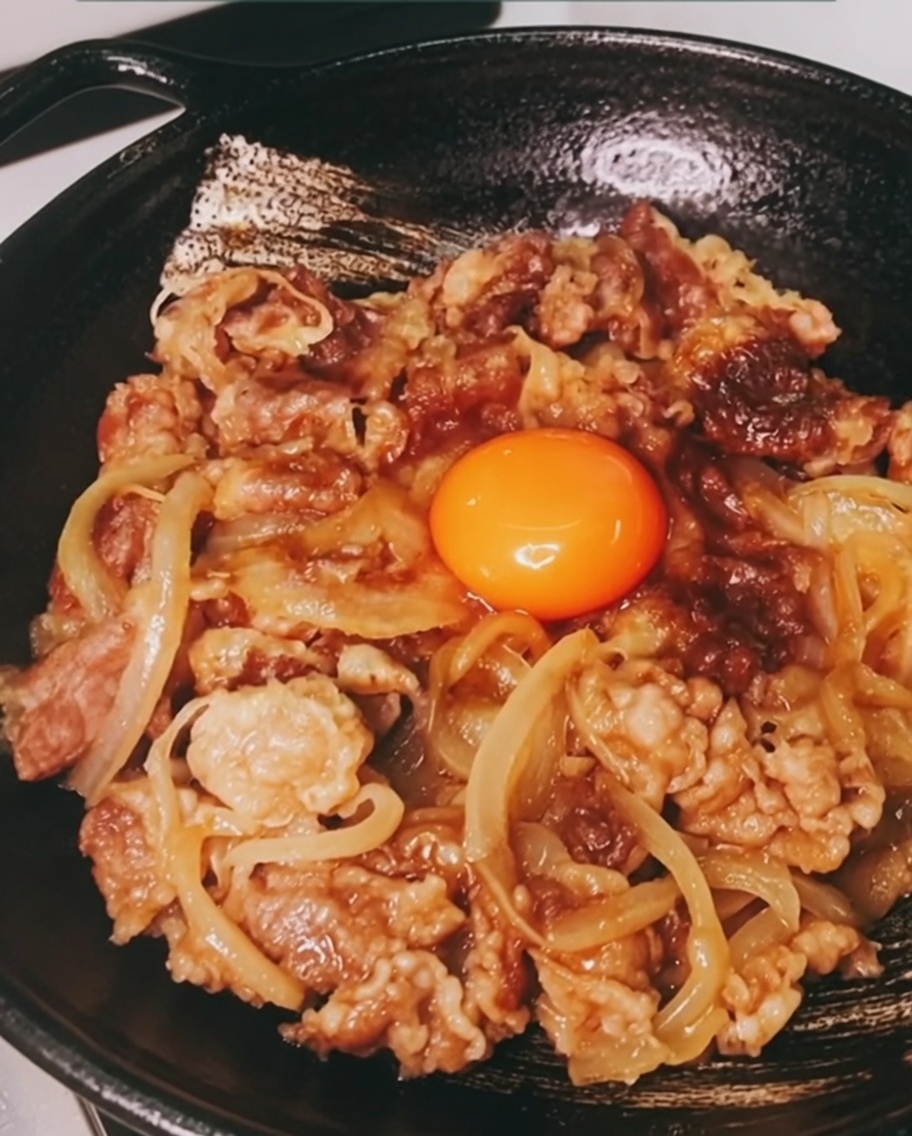 조리된 소고기와 양파 한가운데에 놓인 선명한 주황빛의 날달걀 노른자.