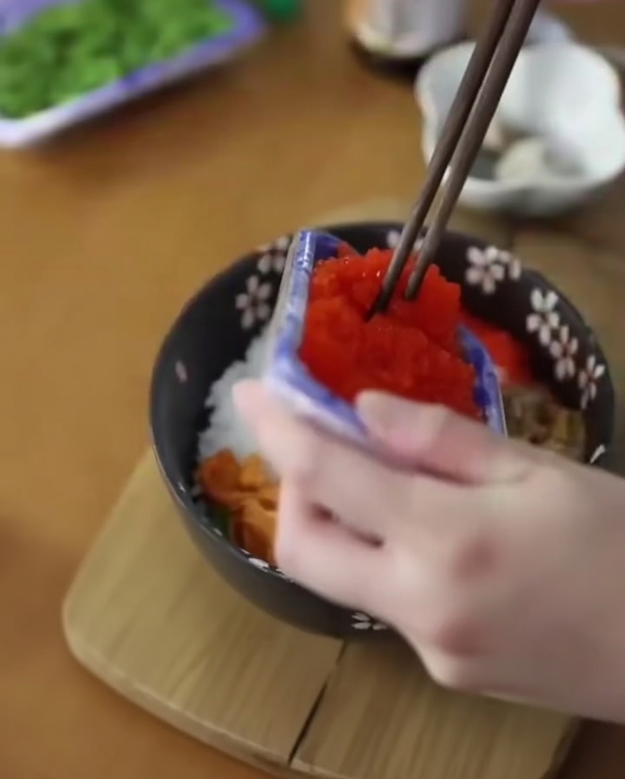이미 성게알이 올려진 덮밥에 주황색 날치알을 추가하는 모습.