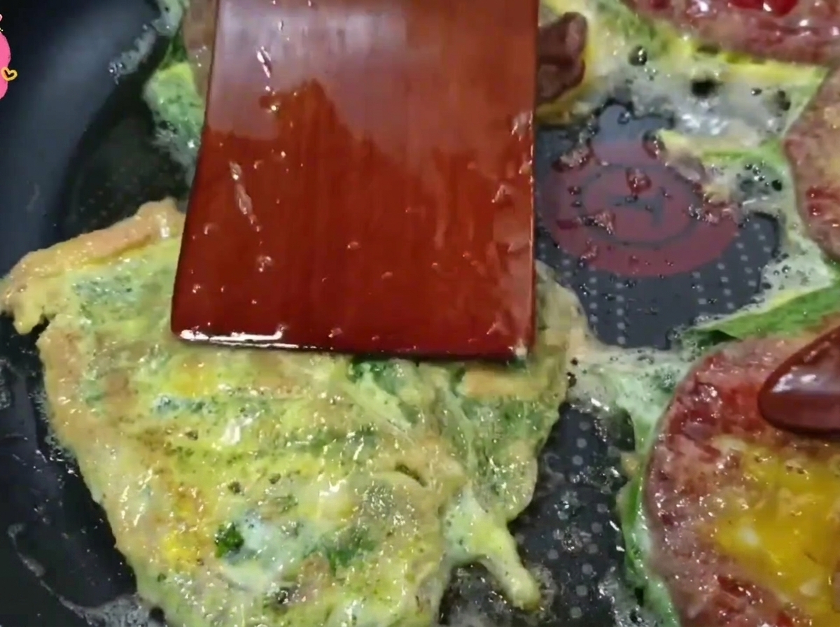 바닥이 황금빛으로 익은 깻잎전을 나무 뒤집개로 뒤집는 모습.