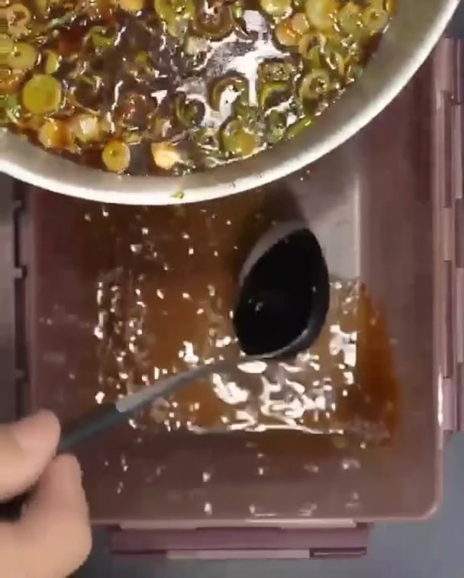 밀폐 용기에 겹겹이 쌓인 갈비 위로 양념장을 붓는 모습.