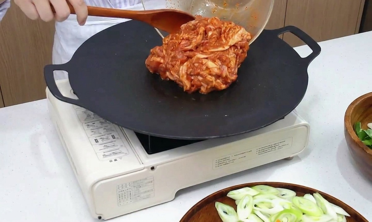 달궈진 검은색 그리들 팬에 양념된 돼지고기를 올리는 모습.