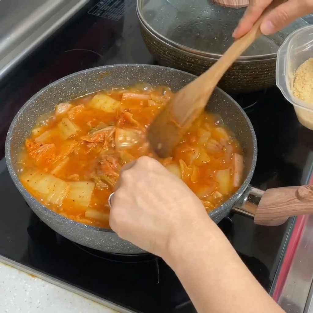 보글보글 끓는 빨간 김치찌개에 다진 마늘 한 숟갈을 섞는 모습.