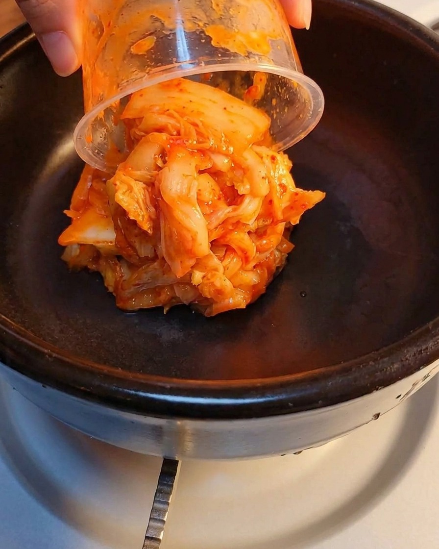 돌솥 안에 신김치와 으깬 런천미트를 층층이 담은 모습.