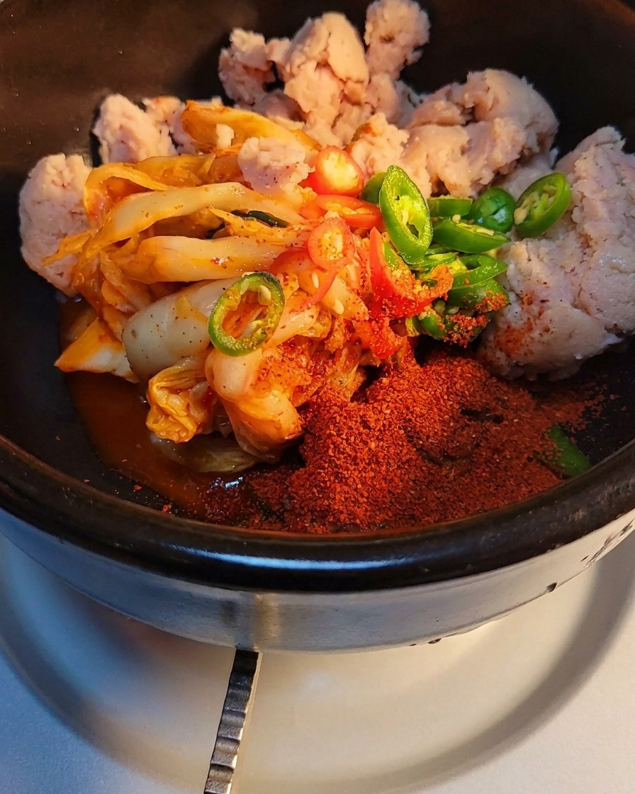 돌솥의 김치와 고기 위로 설탕과 소고기 다시다를 뿌리는 클로즈업 사진.