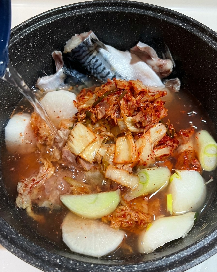 물 아래로 재료들이 보이는 가운데 간장 등 액체 양념을 냄비에 추가하는 클로즈업 모습.