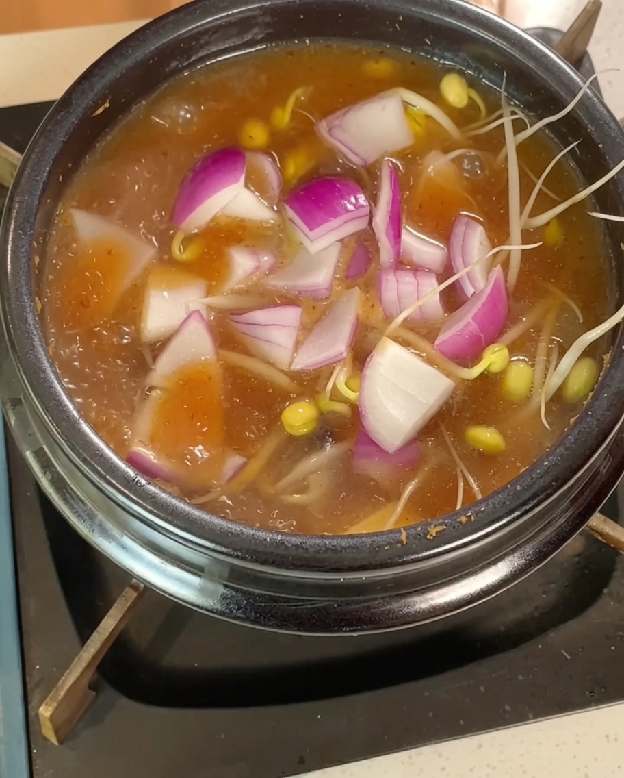 콩나물, 양파, 깍둑썰기한 두부를 끓는 찌개에 넣는 모습.