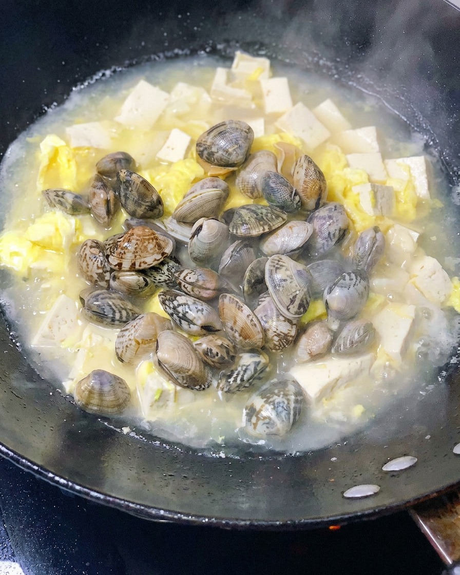 두부와 달걀이 끓는 냄비에 신선한 조개를 넣는 모습.