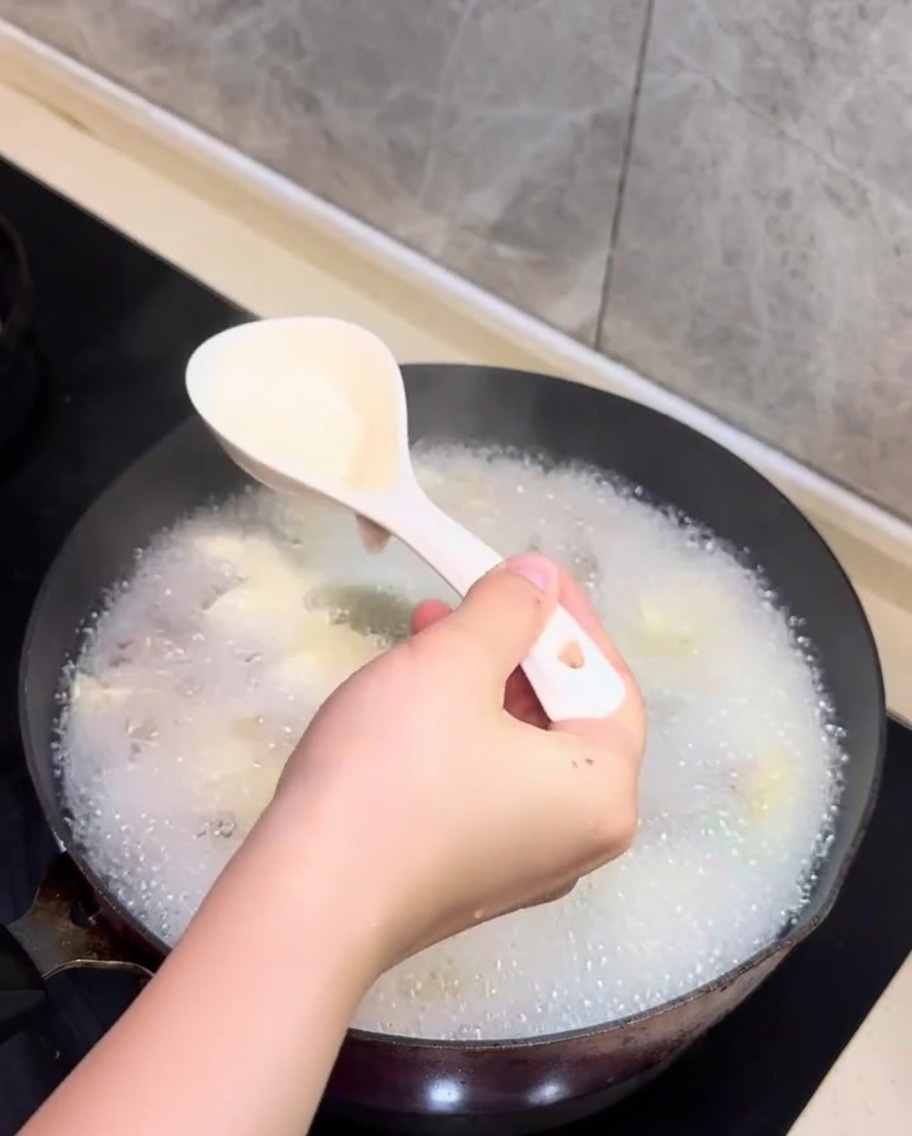 숟가락으로 끓고 있는 국물 위 거품을 걷어내는 모습.