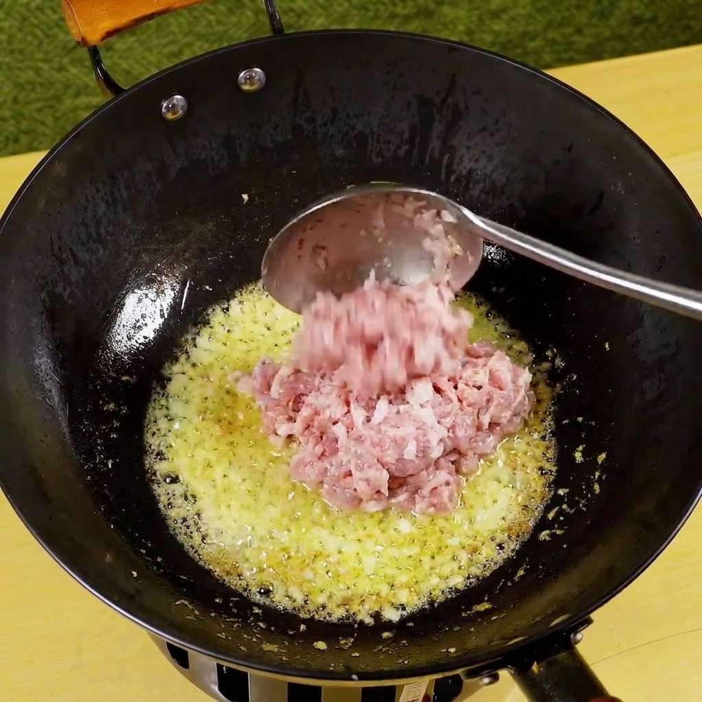 볶은 양파와 마늘이 담긴 팬에 넣어 갈색으로 익어가는 다진 돼지고기.