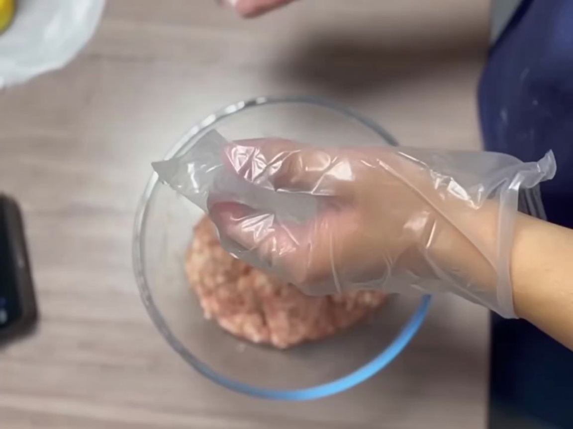 장갑을 낀 손으로 고기 반죽을 단단하고 매끄러운 공 모양으로 만드는 모습.