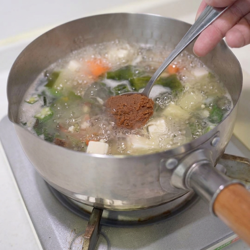 끓고 있는 야채국에 갈색 미소 페이스트를 넣는 모습.