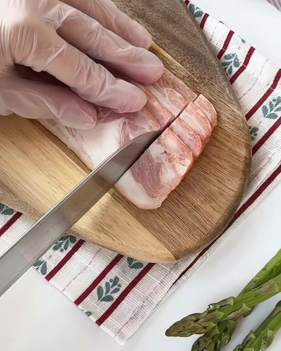 도마 위에서 베이컨을 균일한 사각형 모양으로 썰고 있는 모습.