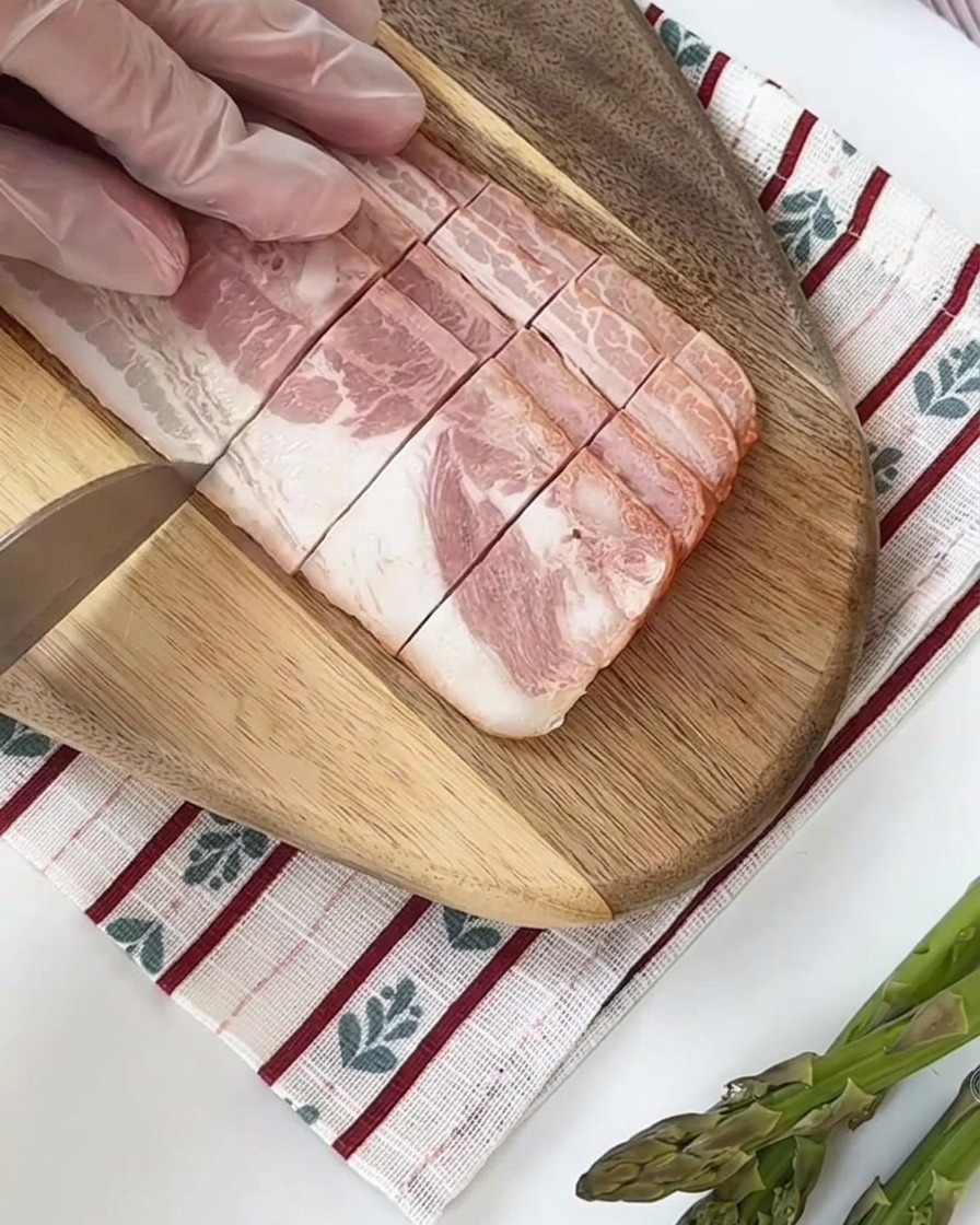 신선한 아스파라거스 줄기를 도마 위에서 일정한 크기로 자르는 모습.