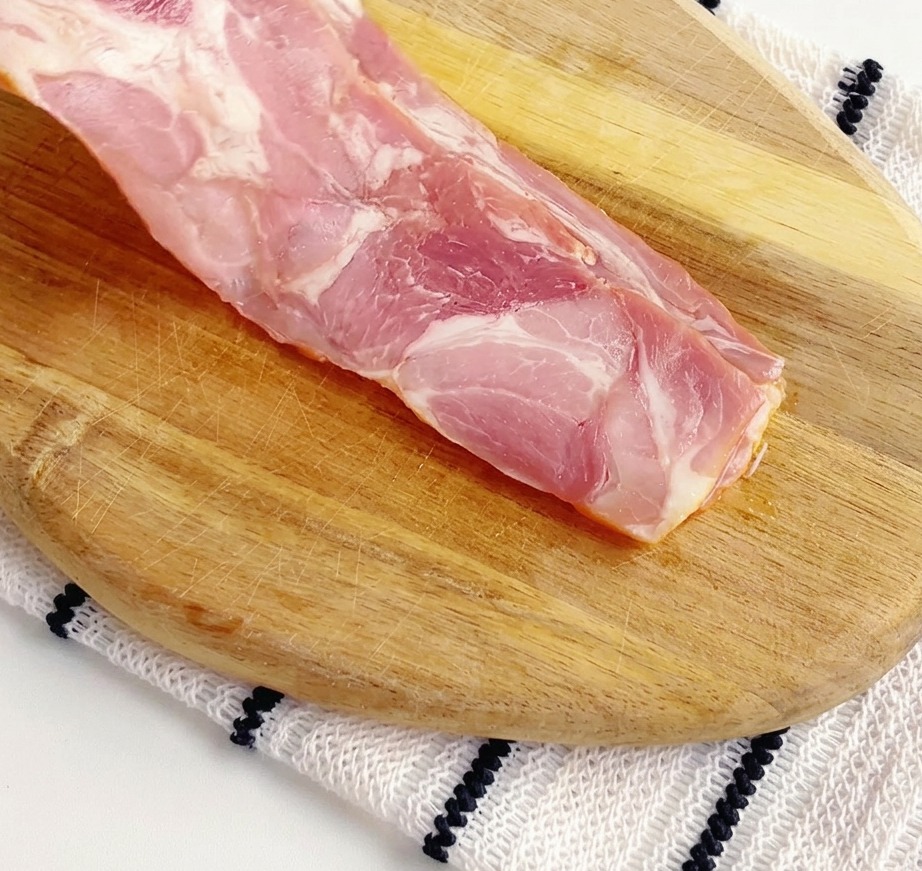 도마 위에서 베이컨을 작은 조각으로 써는 모습.