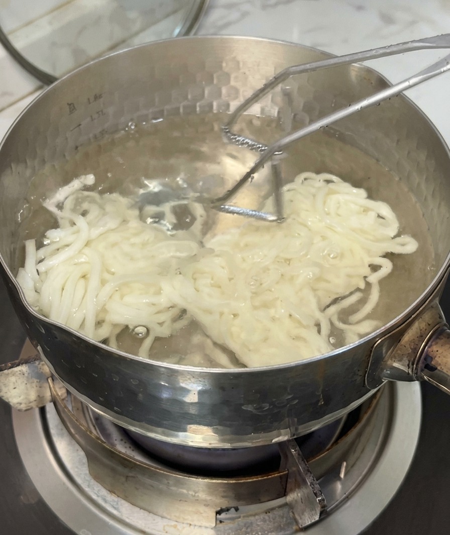 끓는 물에서 우동면을 체로 건져내는 모습.