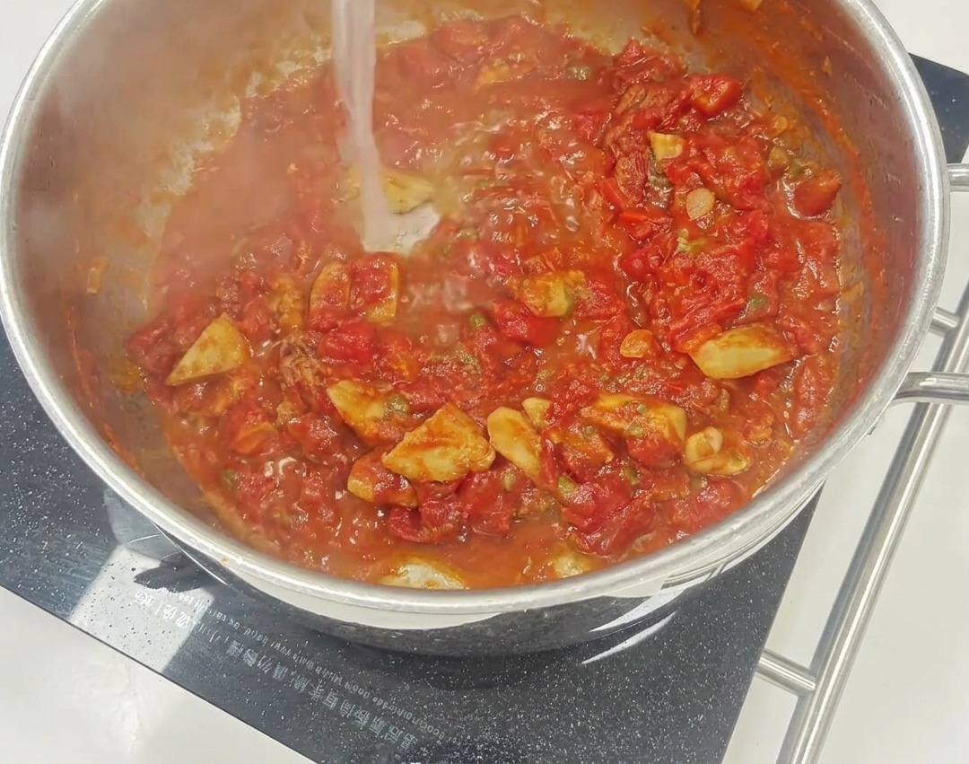 썬드라이 토마토와 케이퍼 조각들이 보이는, 프라이팬에서 보글보글 끓고 있는 선명한 붉은색 토마토 소스
