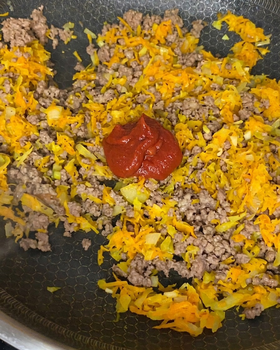 구운 고기, 양파, 당근 혼합물에 토마토 페이스트, 크러시드 토마토, 간장을 넣고 젓는 모습.