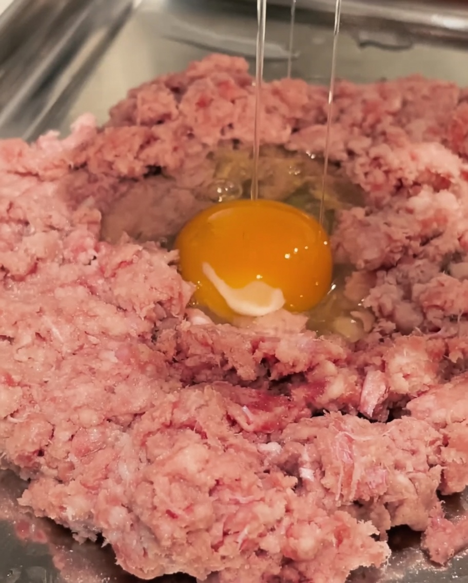 소고기 다짐육이 담긴 볼에 신선한 계란을 깨트려 넣는 모습.