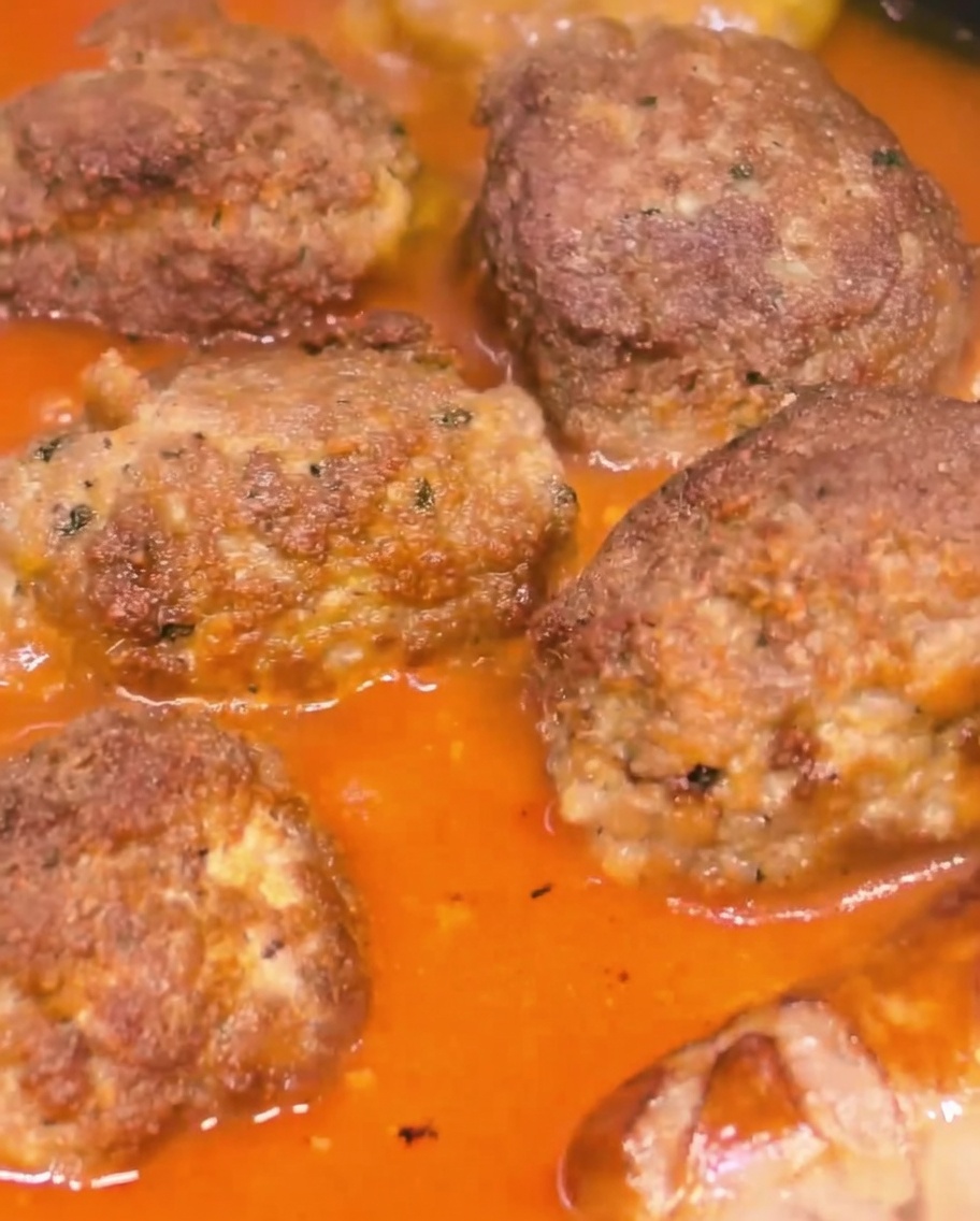 걸쭉하고 진한 토마토 소스에서 큼직한 미트볼과 소시지가 함께 끓고 있는 모습.