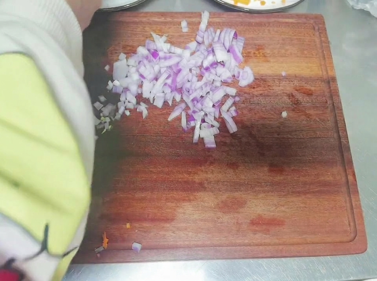 나무 도마 위에서 적양파를 작게 깍둑썰기하는 모습.