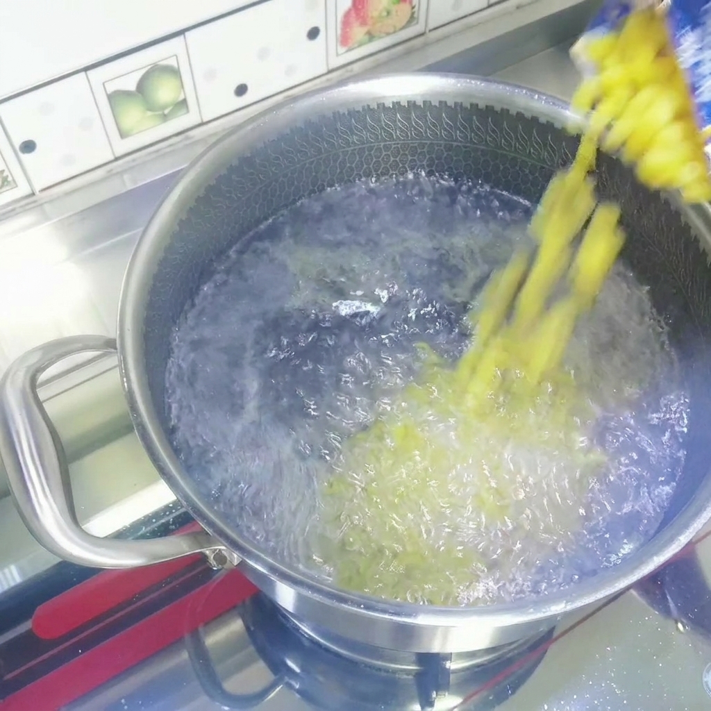 펄펄 끓는 물이 담긴 스테인리스 냄비에 건조 마카로니를 붓는 모습.