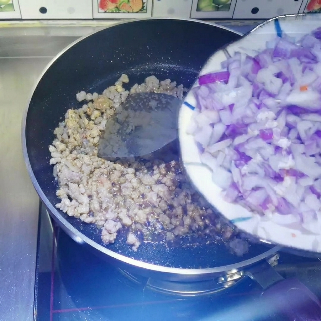 접시에 담긴 다진 적양파를 볶은 고기가 있는 팬으로 옮기는 모습.