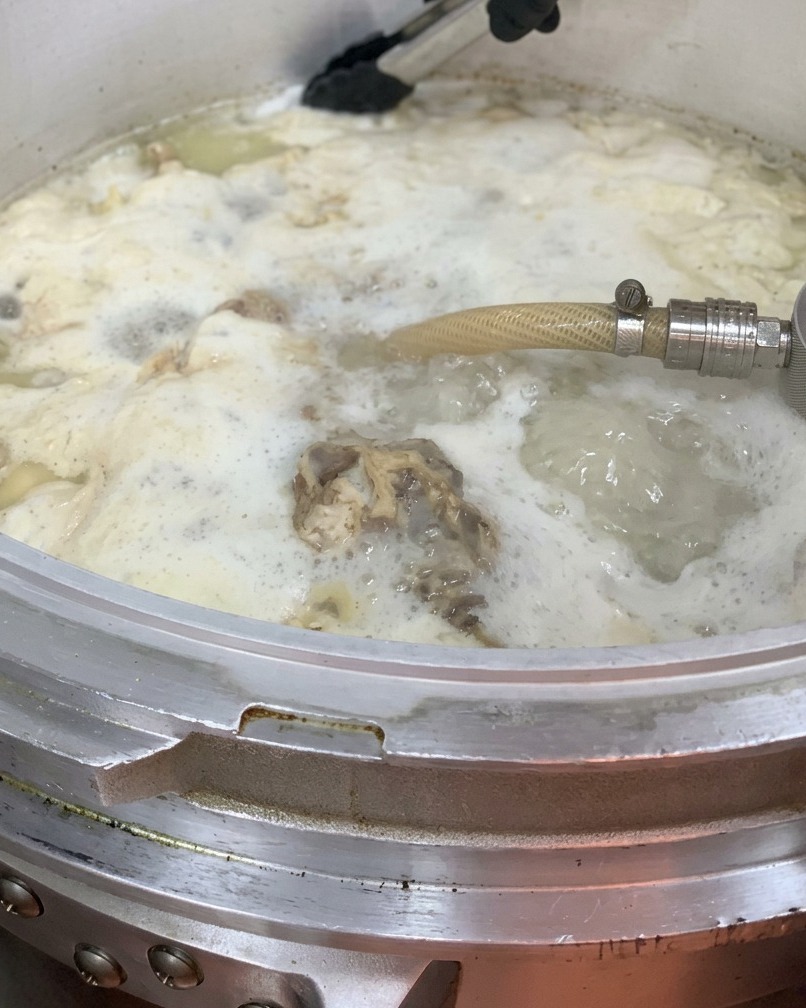 육수가 담긴 큰 냄비에 닭 기름을 붓는 모습.