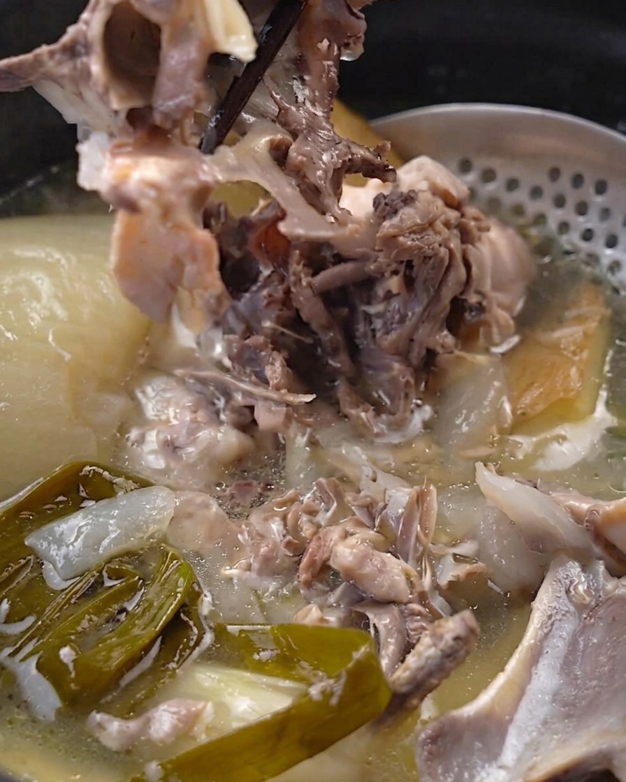 냄비 안에서 젓가락으로 푹 익은 부드러운 닭고기 살을 뼈에서 분리하는 모습
