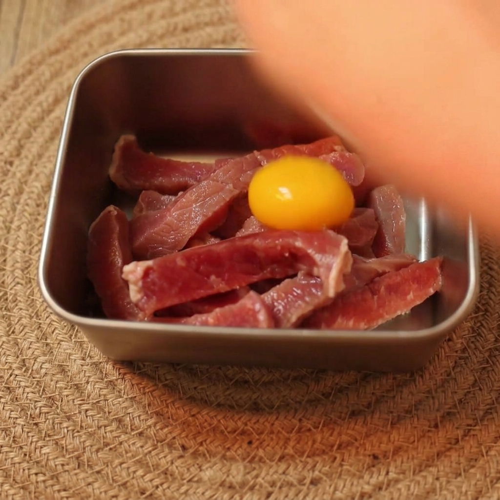금속 볼에 담긴 생고기 위에 밝은 노란색 달걀노른자가 올라가 있는 모습.