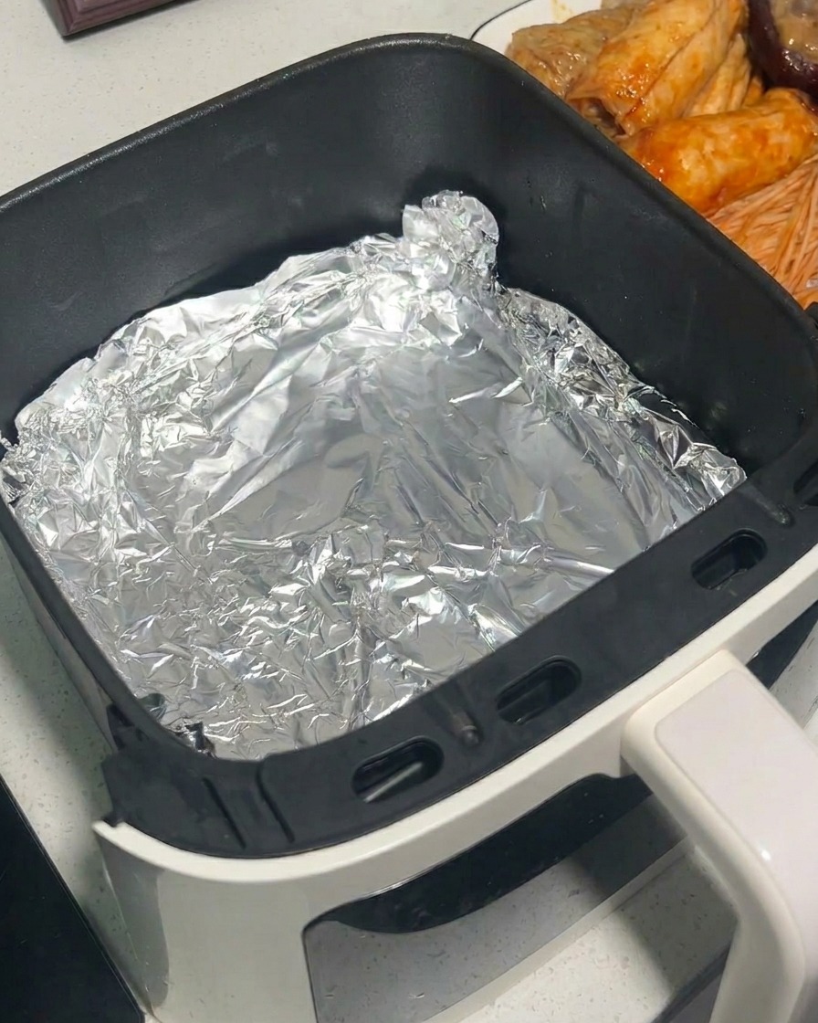 집게를 이용해 양념된 버섯을 알루미늄 포일을 깐 에어프라이어 바스켓에 담는 모습.