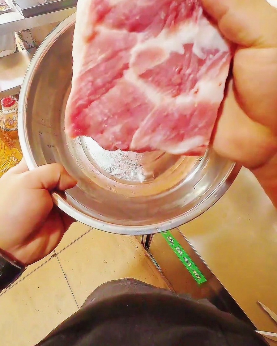도마 위에서 날카로운 칼로 신선한 삼겹살 덩어리를 길게 써는 모습.