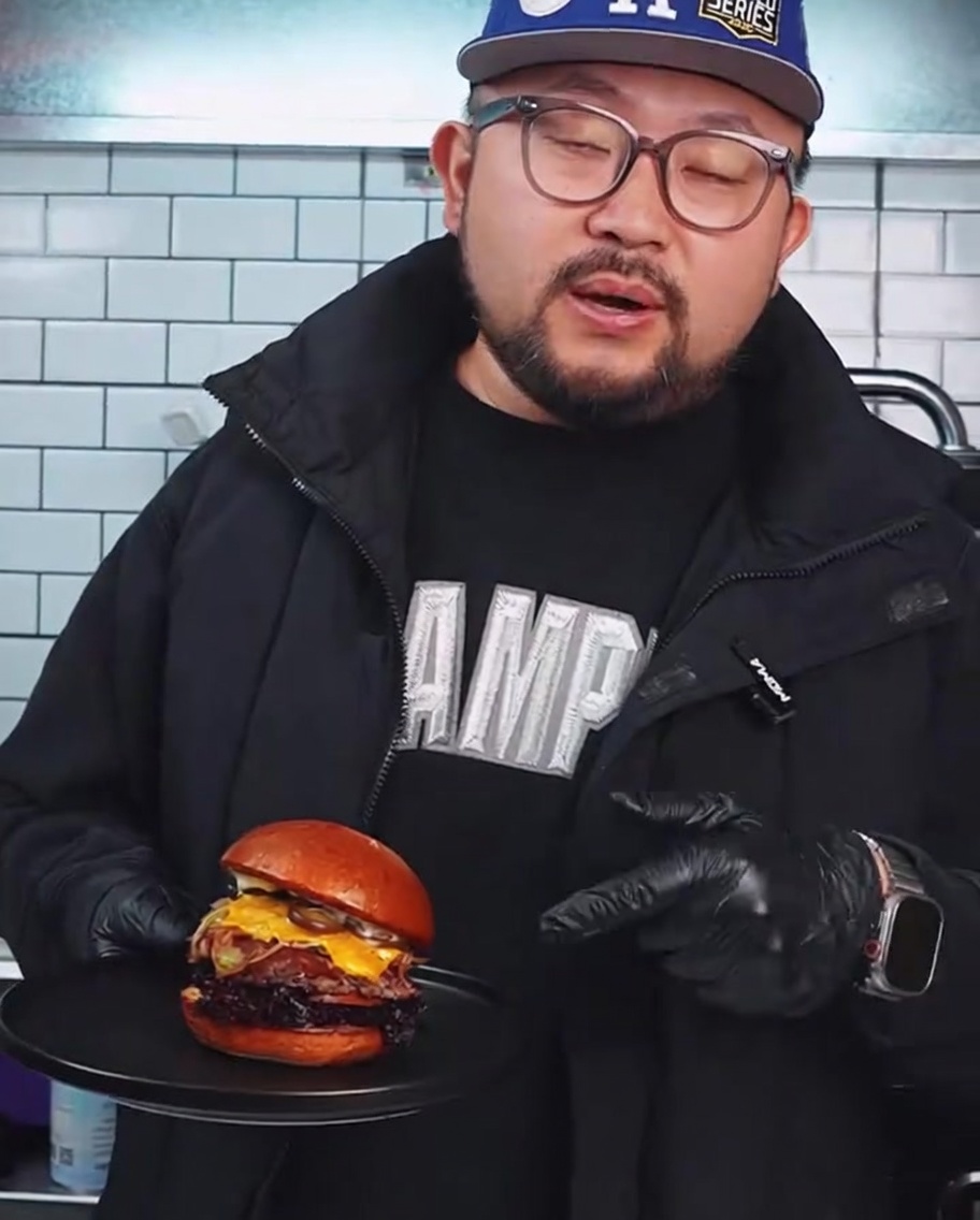 뜨거운 그릴 위에서 무거운 금속 버거 프레스로 와규 패티를 납작하게 누르는 모습.