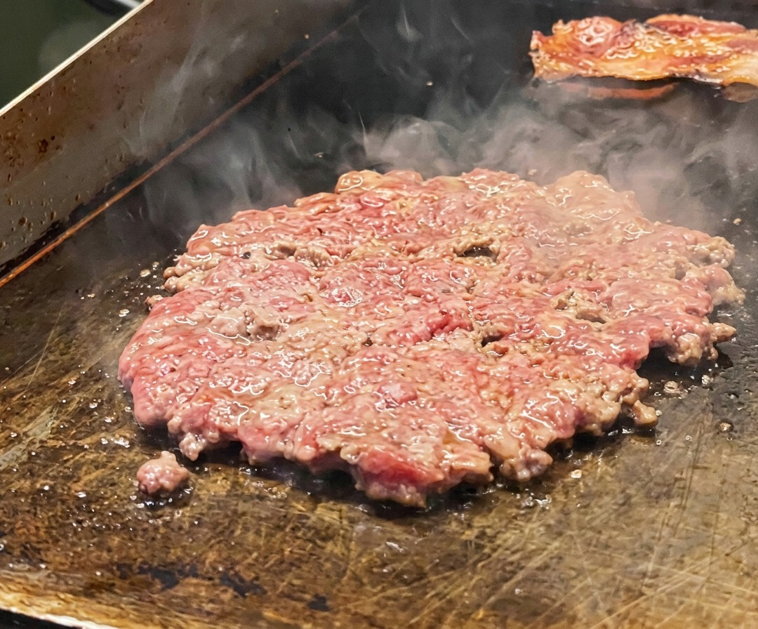 소금으로 간을 하고 양파 슬라이스를 얹어 그리들에서 구워지는 얇은 소고기 패티.
