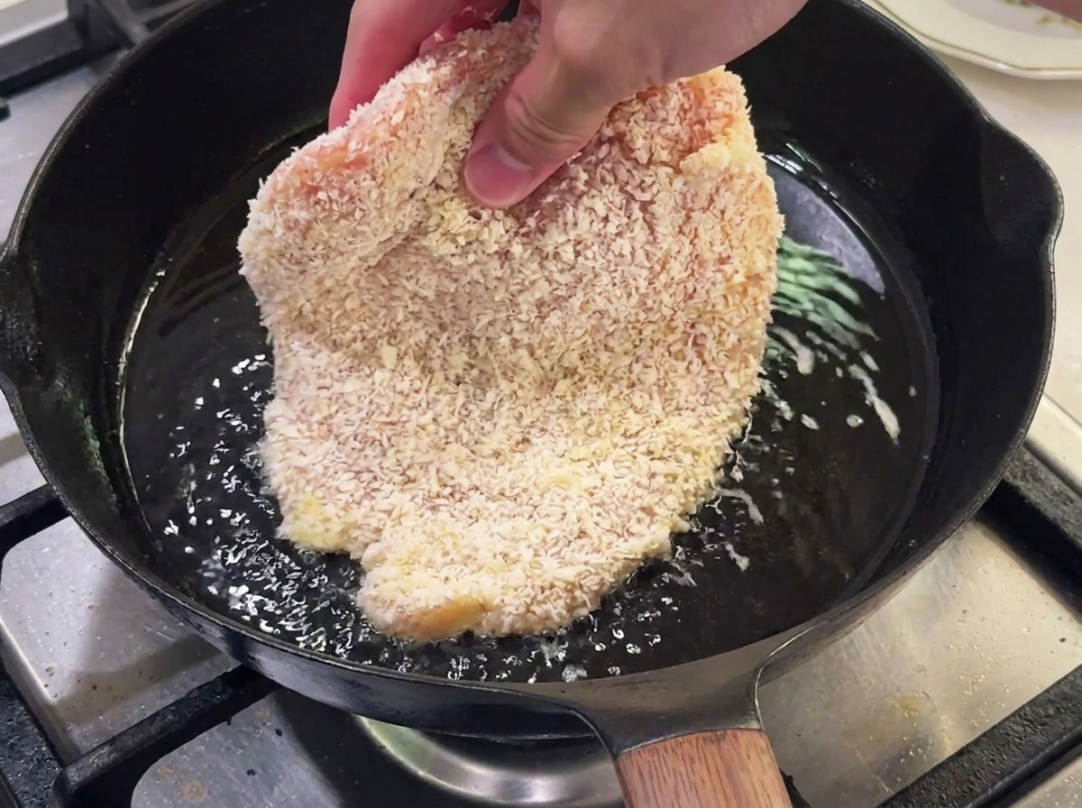 뜨거운 기름이 담긴 팬에서 빵가루 입힌 닭고기를 튀기는 모습.