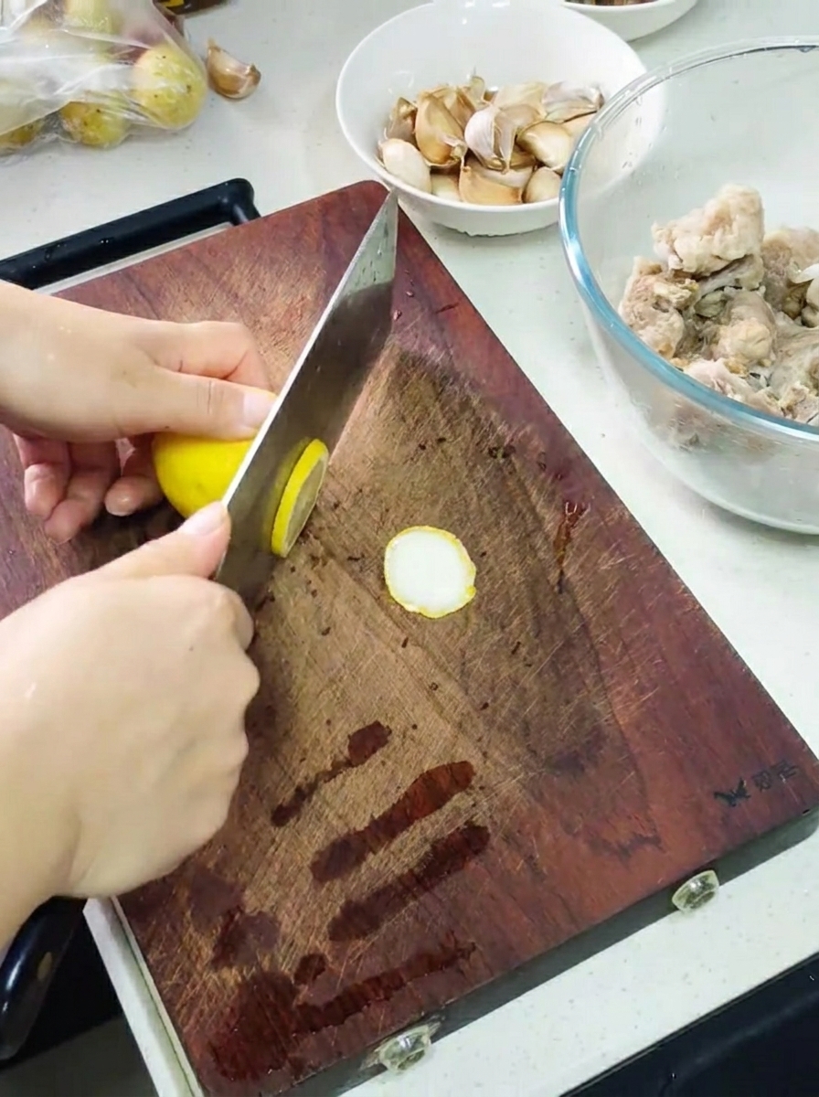 도마 위에서 칼로 레몬을 슬라이스하고, 옆에는 양념에 재운 갈비와 마늘이 담긴 볼이 놓여 있음.