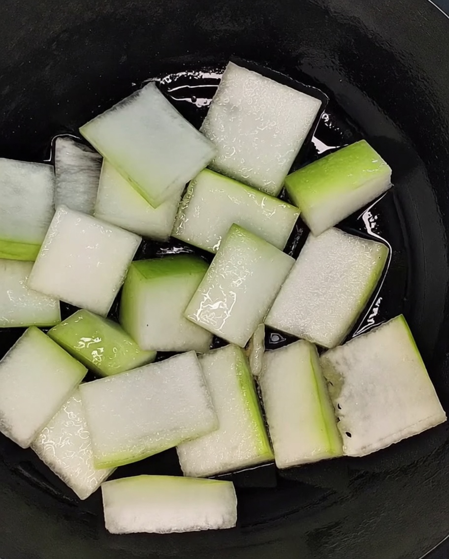 검은색 냄비 바닥에 동아 조각을 고르게 배치한 모습.