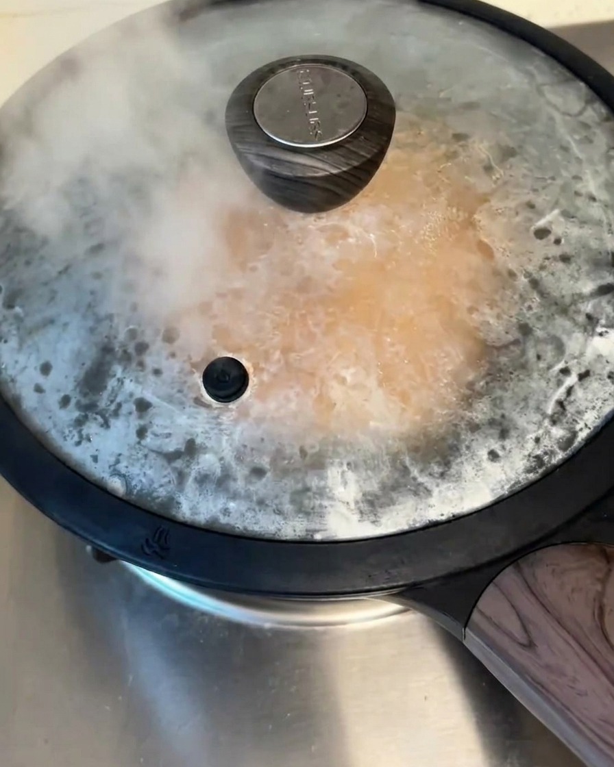 가스레인지 위에 뚜껑을 덮은 팬이 있고 파전이 익어가는 동안 뚜껑 틈으로 수증기가 빠져나오는 모습.