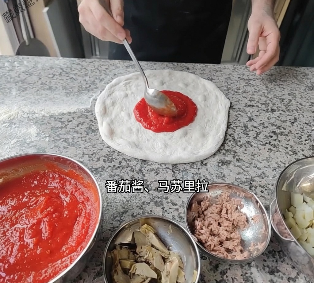 국자를 이용해 작업대 위의 피자 도우 베이스에 매끄러운 빨간색 토마토 소스를 펴 바르는 모습.