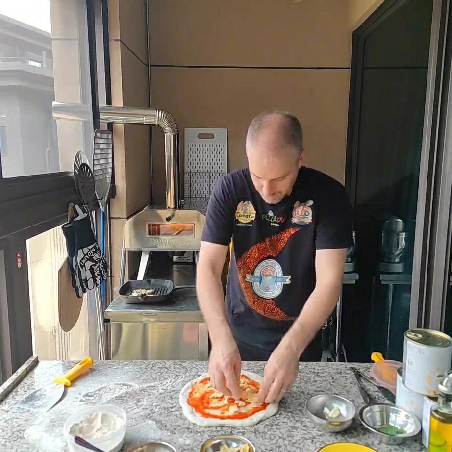토마토 소스가 발린 피자 도우 위에 잘게 썬 모짜렐라 치즈를 뿌리는 모습.