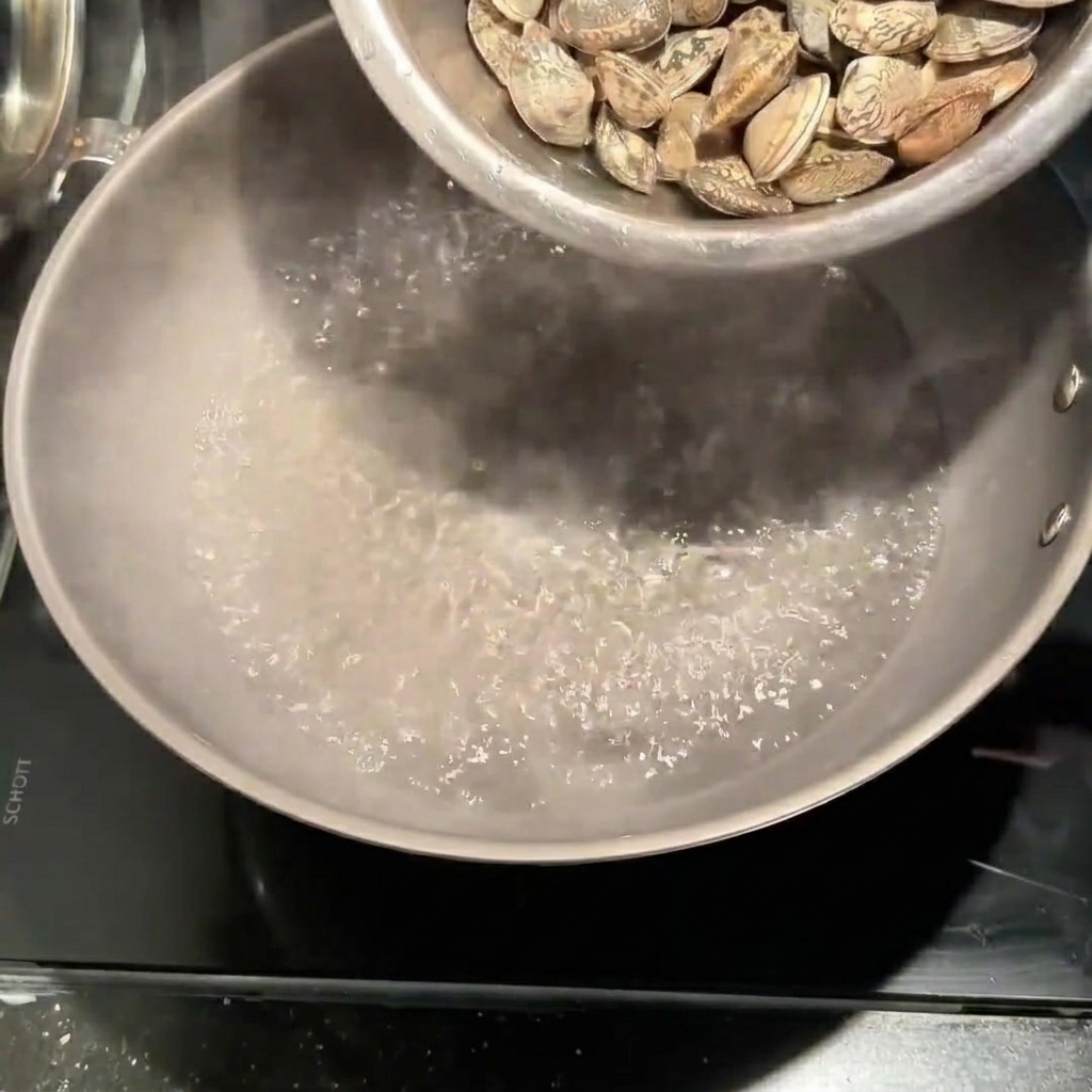 소금을 넣고 끓는 물이 담긴 냄비에 신선한 바지락을 붓는 모습.