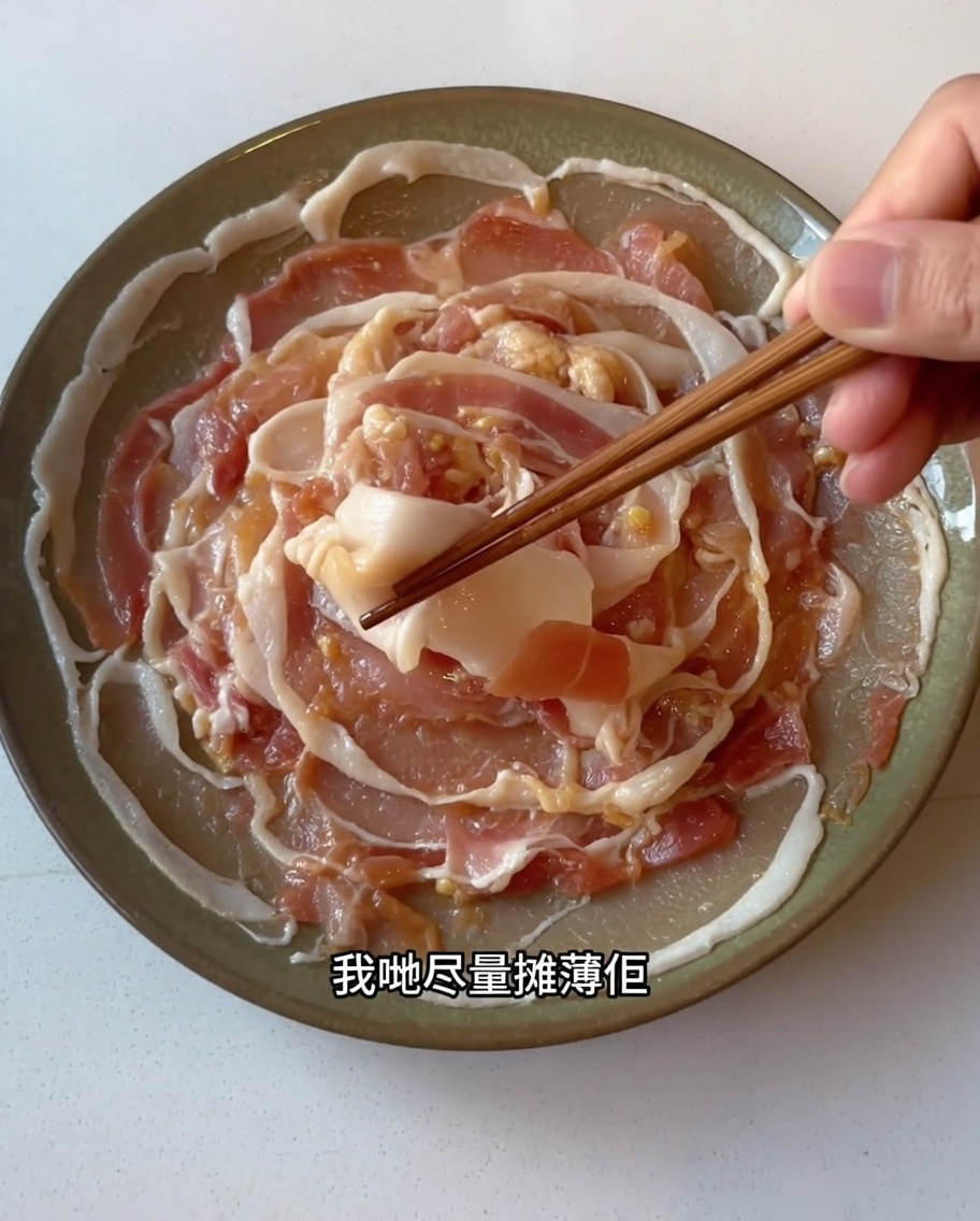 젓가락을 사용하여 양념한 삼겹살을 접시에 겹치지 않게 펼쳐 담는 모습.