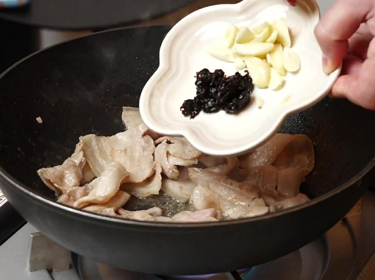 볶은 삼겹살에 마늘과 흑콩을 넣는 모습.