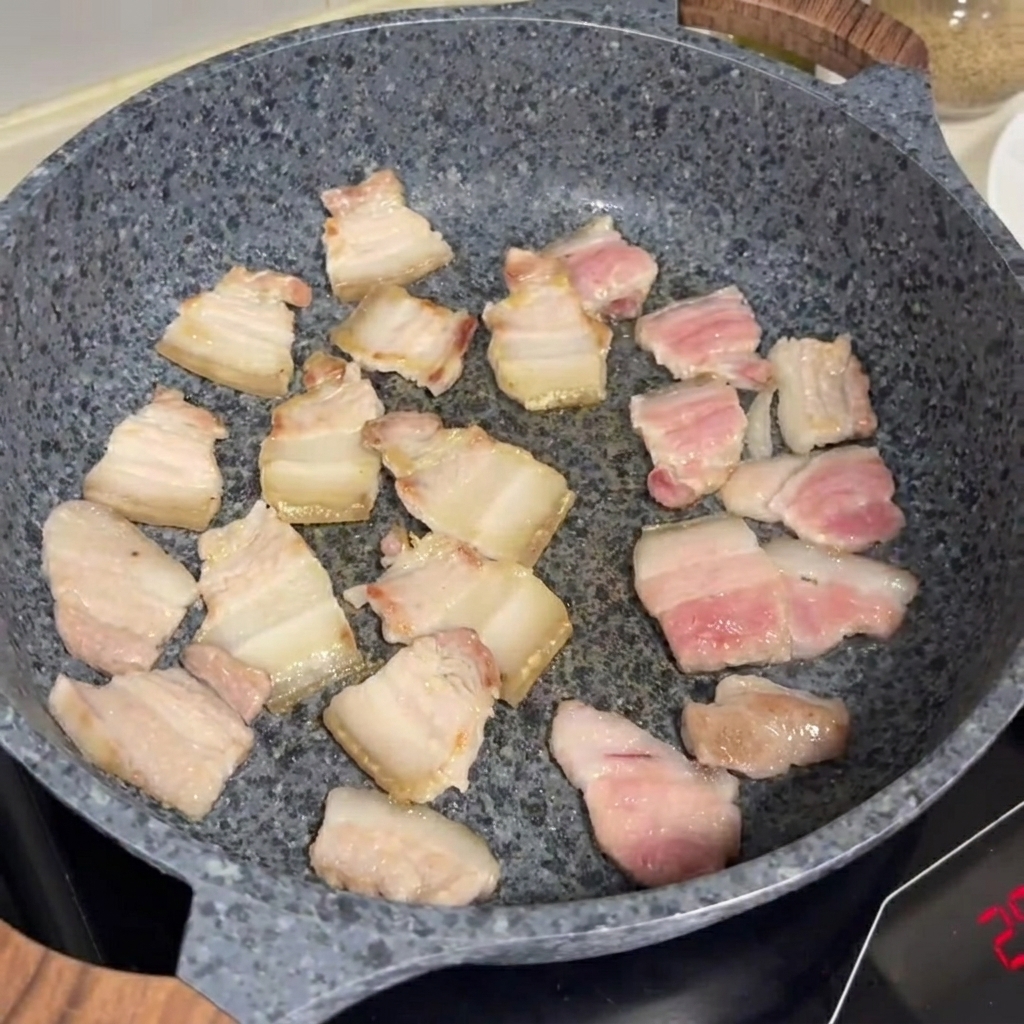 회색 돌솥 팬에서 삼겹살 조각들이 노릇하게 익어가는 모습.
