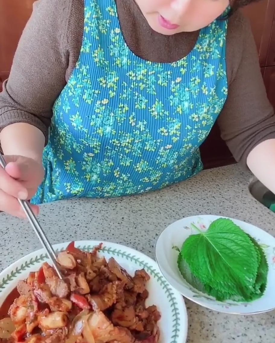 젓가락을 사용하여 익은 삼겹살과 오징어를 신선한 깻잎 위에 올리는 모습.
