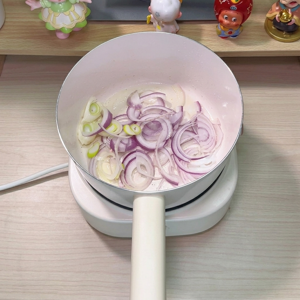 참치 기름에 윤기가 흐르는 양파와 대파를 냄비에서 볶는 모습.