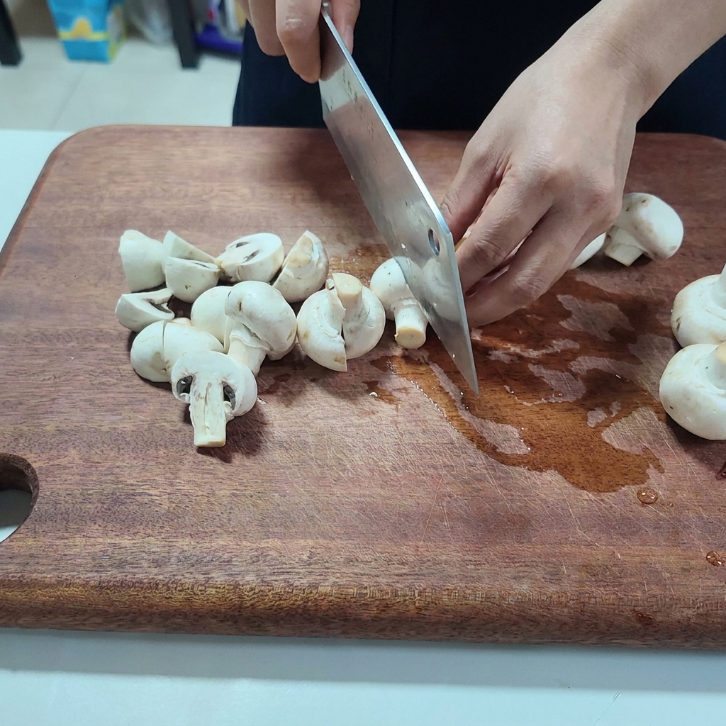 나무 도마 위에서 흰 양송이버섯을 반으로 자르는 모습.