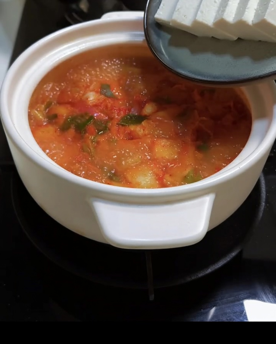 보글보글 끓는 빨간 국물에 두부를 조심스럽게 넣는 모습.